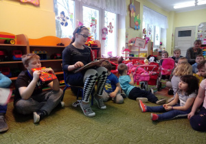Dzieci siedzą na dywanie i słuchają bajki czytanej przez dziewczynkę